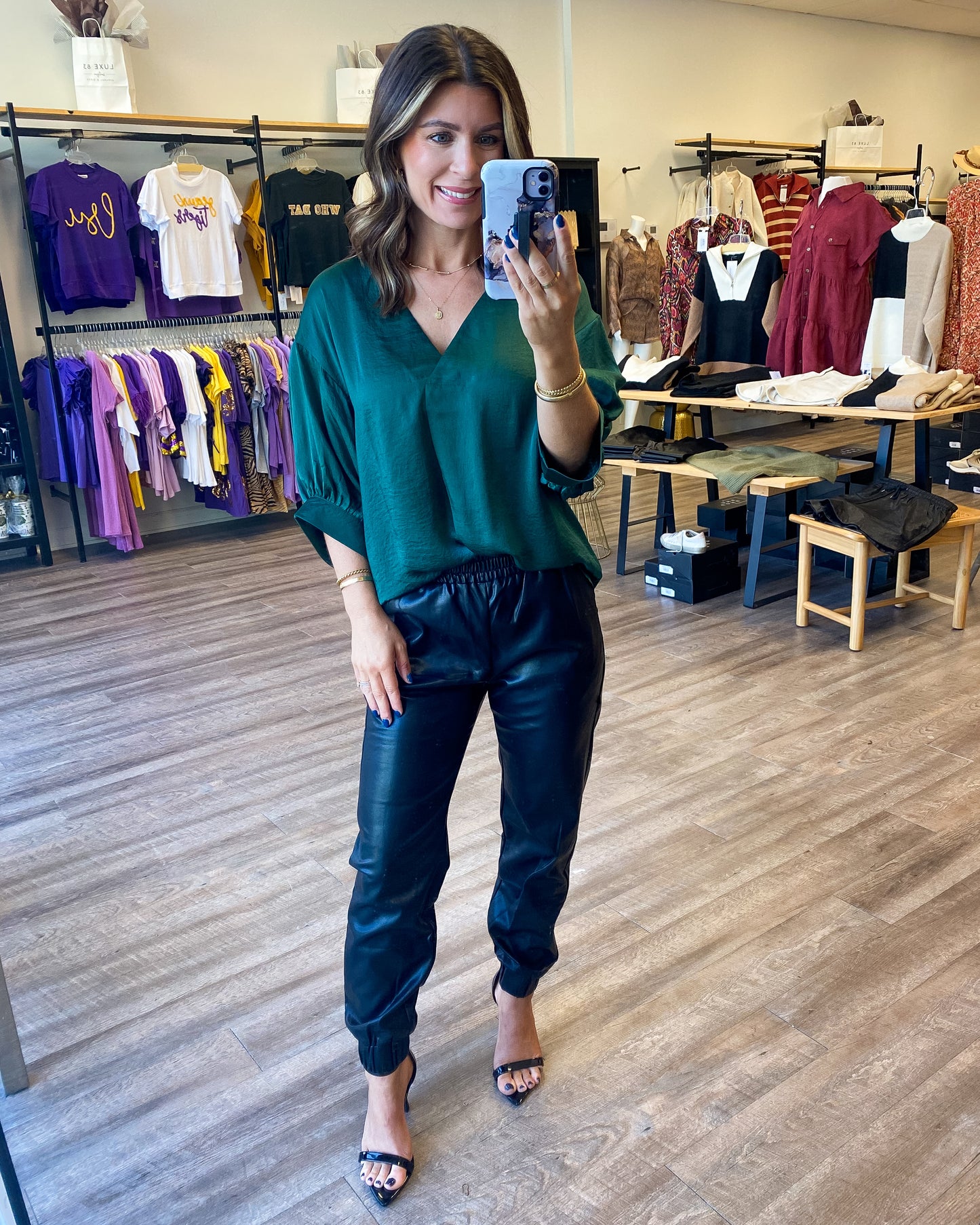 Model is photographed wearing a dark forest green silky blouse with a vneck and short balloon style sleeves. The top is availbale from Luxe 83 Boutique in green and black.