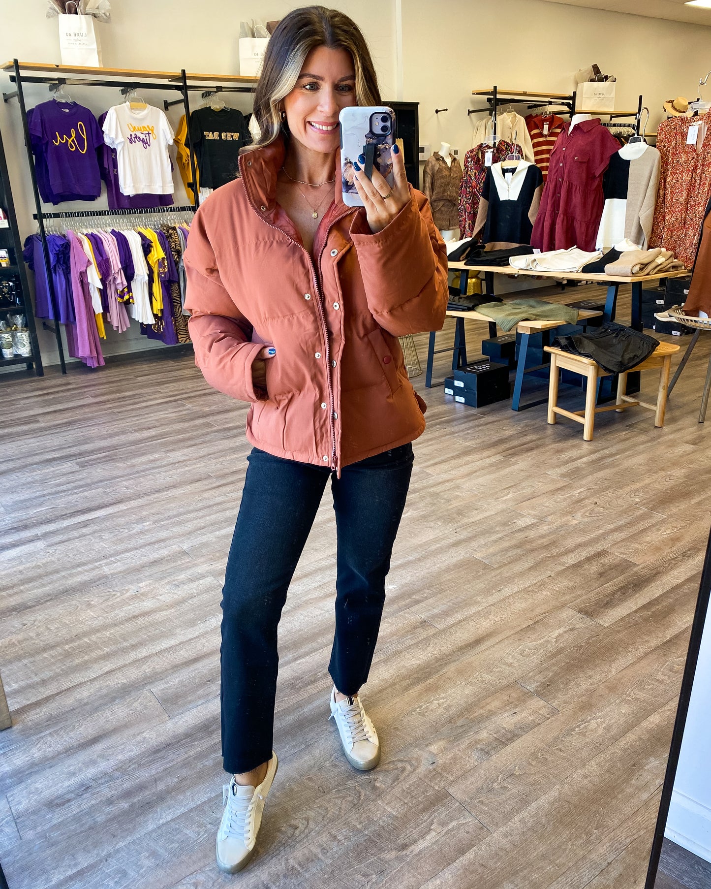 Model is photographed wearing a rust colored puffer style jacket with button and zipper front.