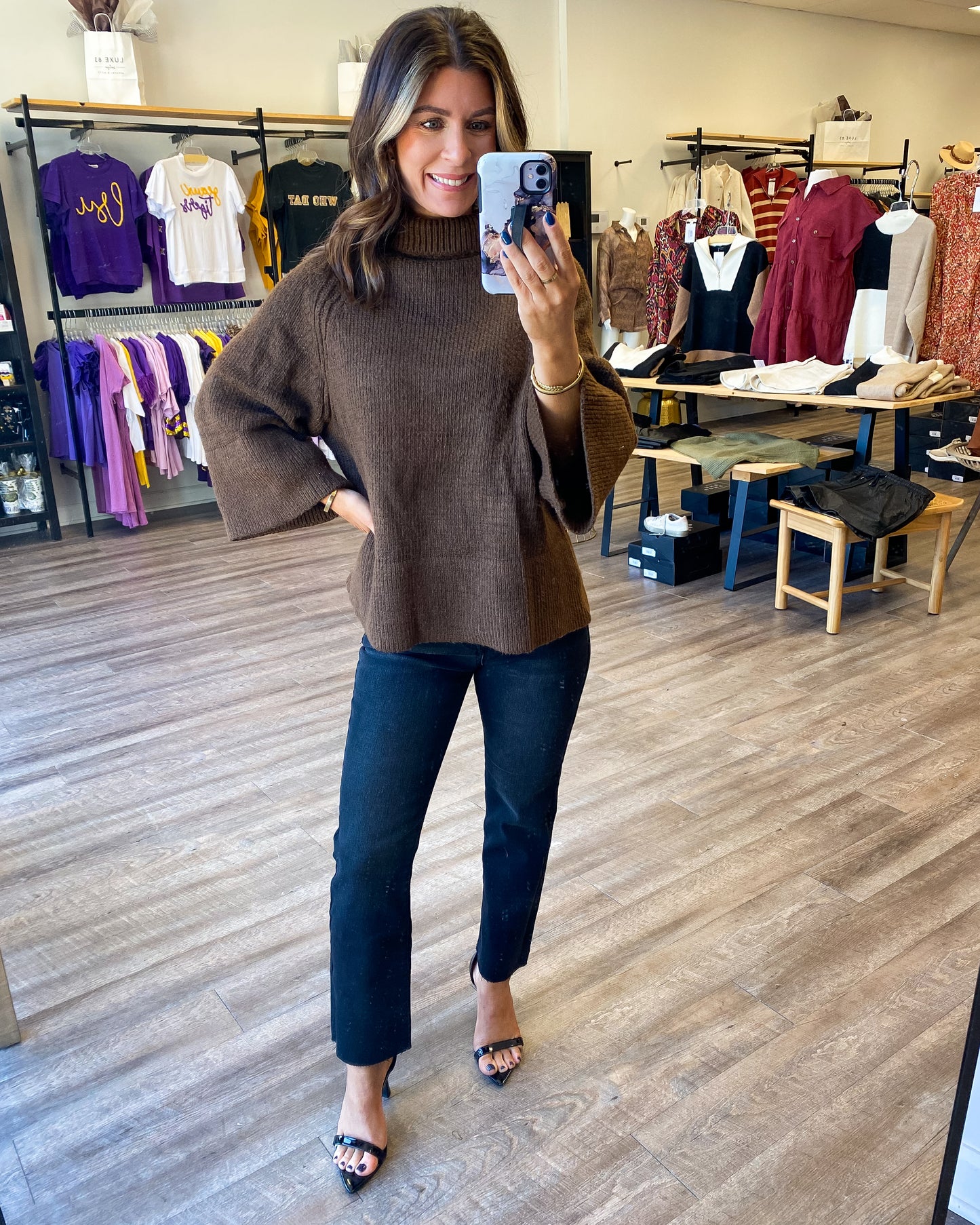 Model is photographed wearing a chocolate colored sweater with 3/4 length sleeves and turtleneck. Model has it paired with black washed denim and black high heels.