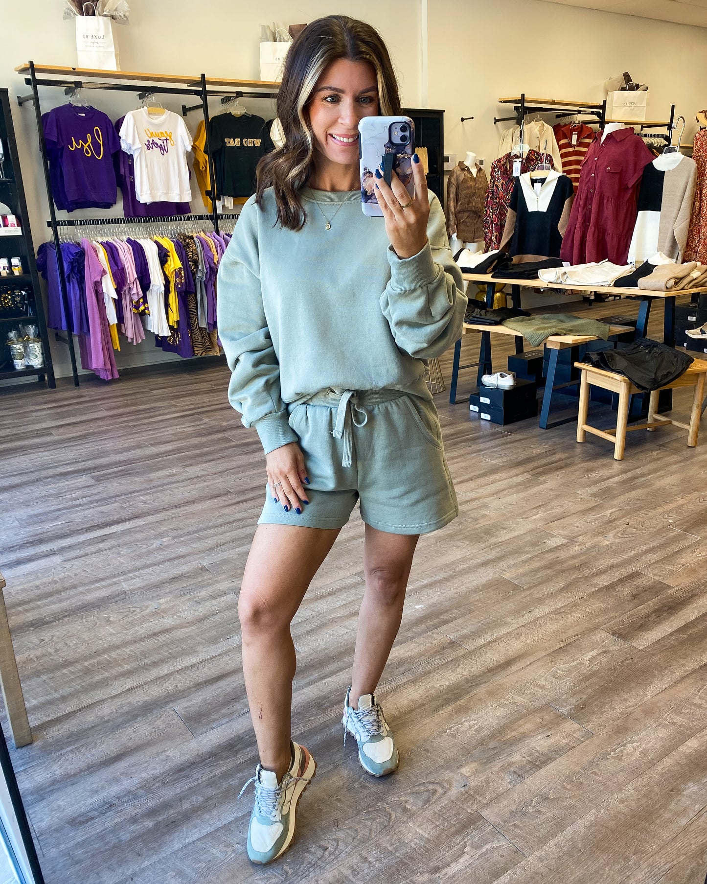 Model is wearing a matching lounge set from Luxe 83 Boutique. The loungeset is a sage green color. It has a long sleeve sweatshirt and shorts with a drawstring waist.