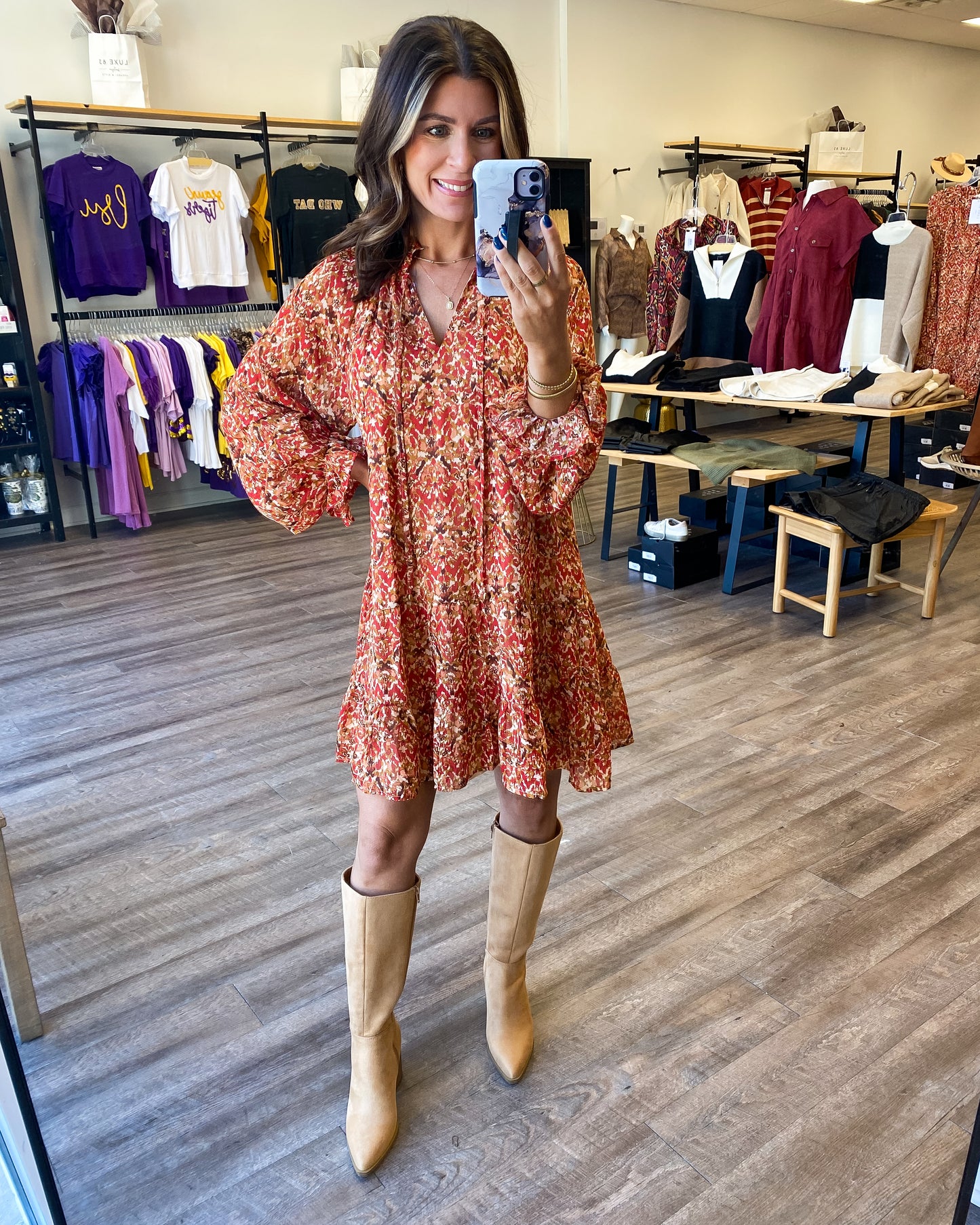 Model is photographed wearing a printed shift dress paired with knee high boots. The dress would be a great Thanksgiving outfit. The colors are orange tones that are perfect for Fall.
