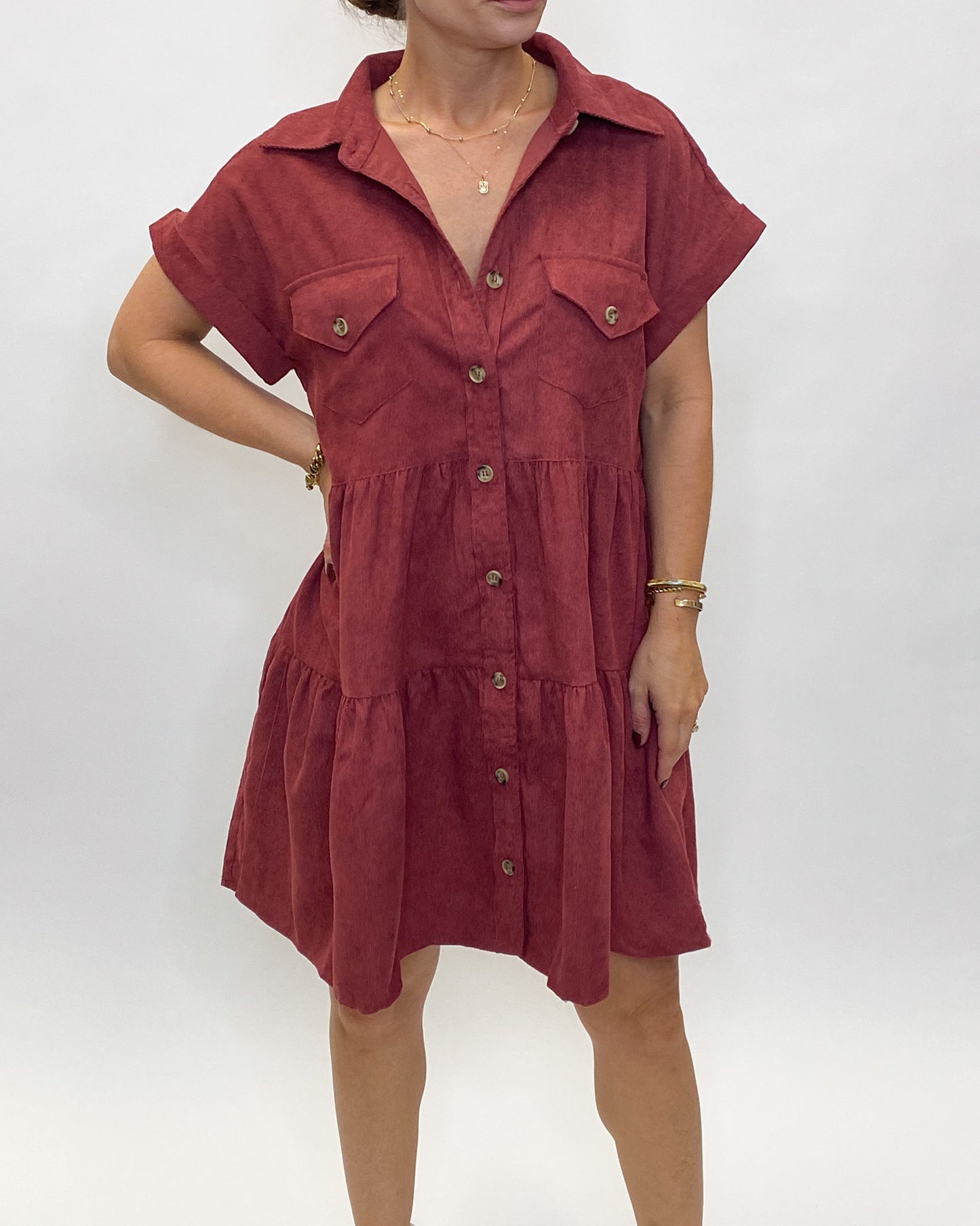 A merlot or wine colored corduroy dress with a babydoll style fit. The dress is a button front and is tiered.