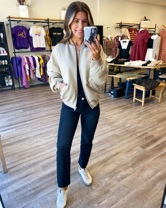 Model is photographed wearing a lightweight bomber jacket with a quilted embroidery pattern in a light tan color.